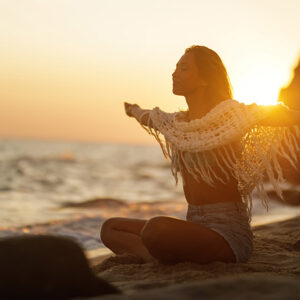 Sorglose Frau mit ausgestreckten Armen, die die Freiheit genießt, während sie sich am Sandstrand bei Sonnenuntergang entspannt