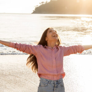 freudige Frau umarmt den Sonnenaufgang am Strand