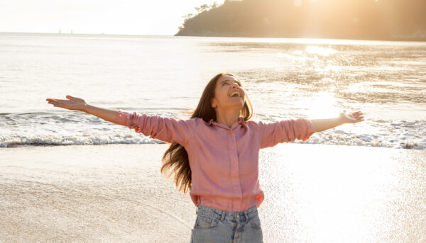 freudige Frau umarmt den Sonnenaufgang am Strand