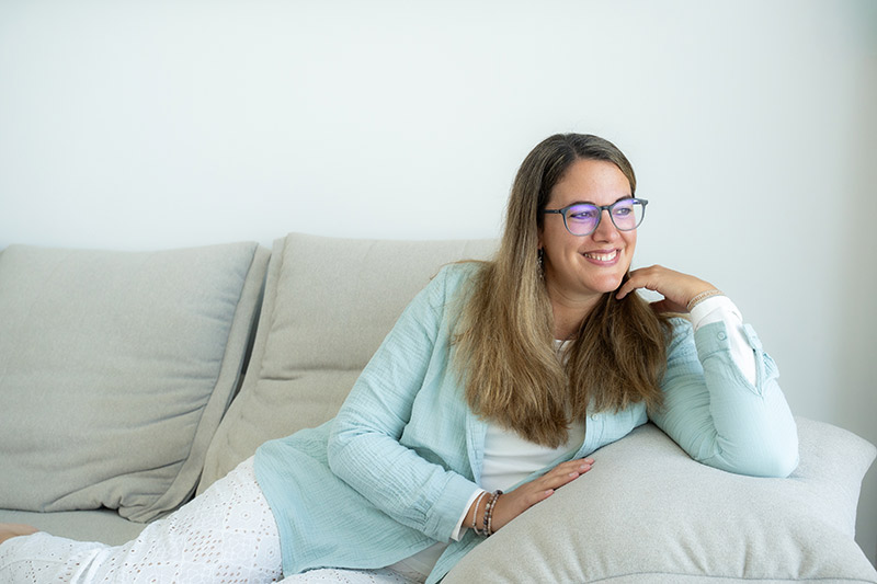 Melanie sitzt auf einer Couch und schaut in die Ferne