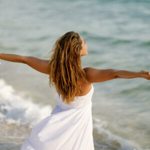 Rückansicht einer Frau, die sich frei fühlt, während sie mit ausgestreckten Armen am Meer steht. Rückansicht einer Frau, die sich frei fühlt, während sie mit ausgestreckten Armen am Meer steht.